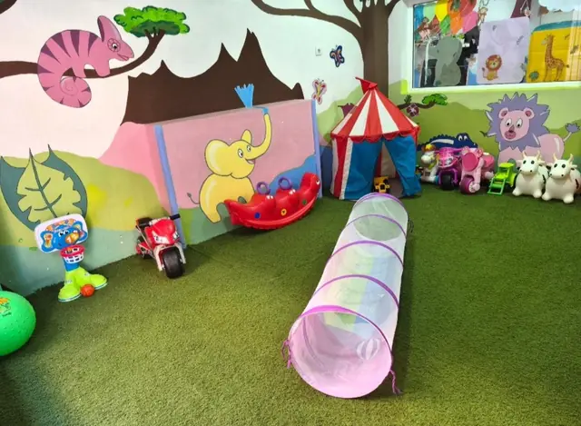 Zona de juego con césped, túnel, carpa y un mural de animales